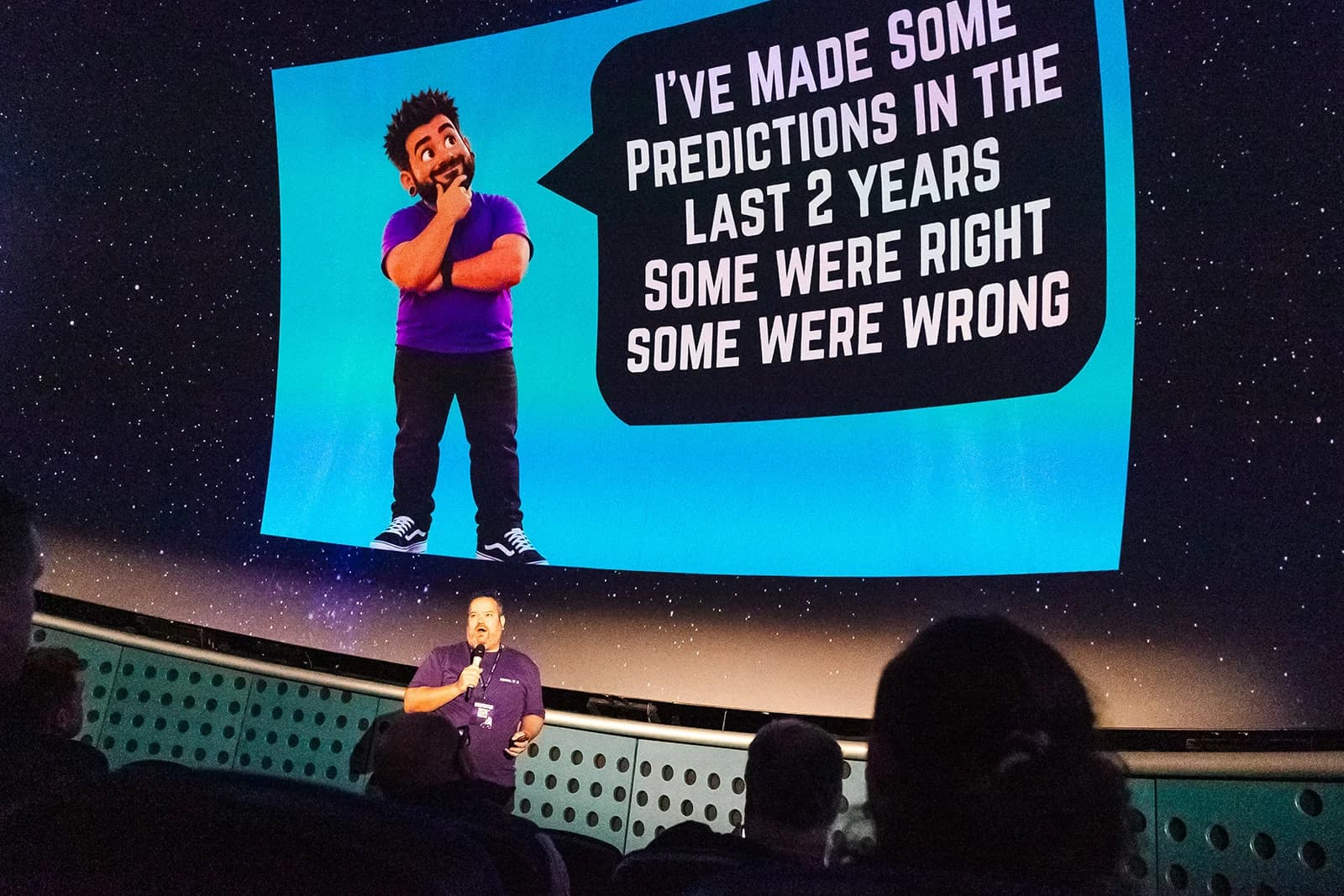 Matt speaking under the planetarium dome at Festival of AI, with a slide behind about predictions made over the last two years